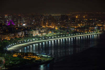 Illuminated cityscape by river against sky at night