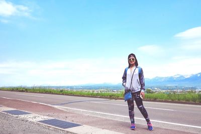 Woman standing on road against cloudy sky