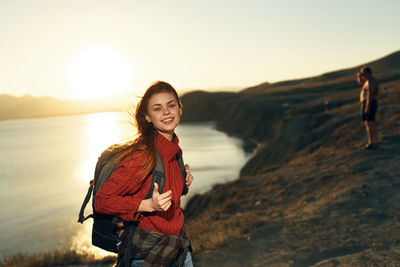 Portrait of smiling young woman standing against sky during sunset