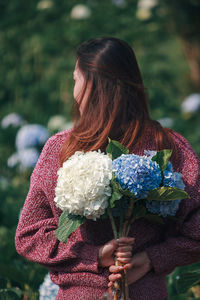 Rear view of woman holding flowers while standing by plants