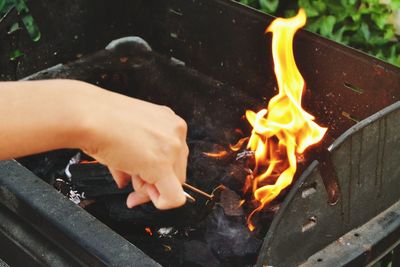 Cropped hand by burning coal in barbecue