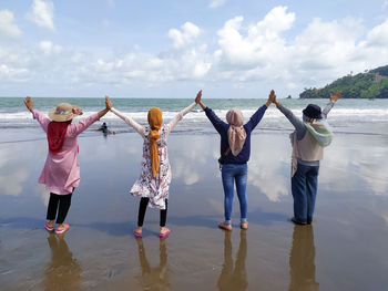 Rear view of women standing at sea shore against sky