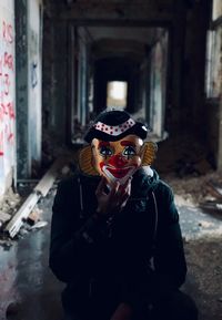 Portrait of mid adult man wearing clown mask while sitting in abandoned building