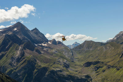Modern helicopter flying over mountain range against cloudy blue sky on sunny day in pyrenees