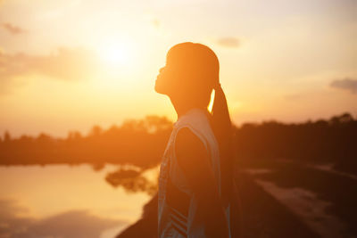 Side view of silhouette woman standing at beach against sky during sunset