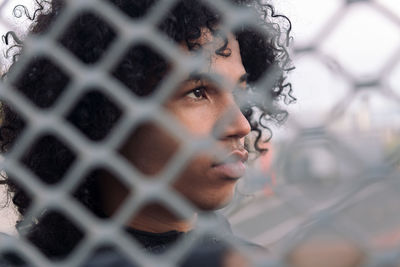 Close-up portrait of young man looking through fence