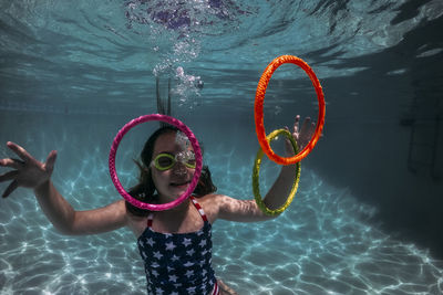 Smiling girl wearing swimming goggles while playing with colorful rings in pool