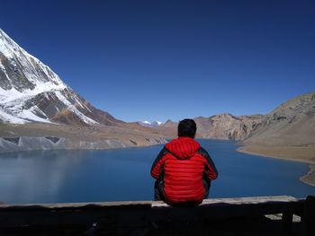 Rear view of man sitting on bench by lake against clear sky