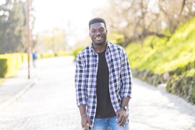 Portrait of smiling young man standing on footpath in park