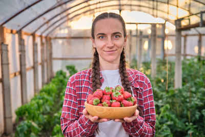 Portrait of young woman holding fruits in greenhouse