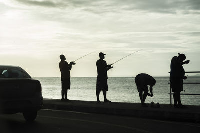 Silhouette people fishing by sea against sky