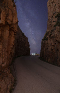 Road amidst rocky mountains against sky at night