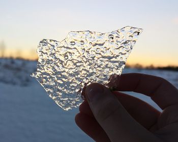 Close-up of hand holding ice against sky