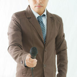 Midsection of man holding camera while standing against white background