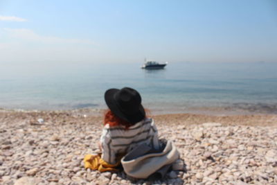 Rear view of man sitting on beach against sky