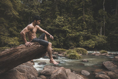 Shirtless man sitting against trees at forest