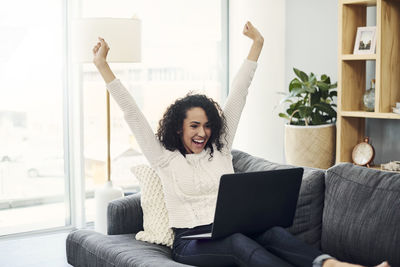 Young woman using phone while sitting on sofa at home