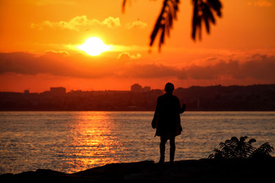 Rear view of silhouette man standing by sea against orange sky