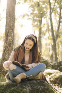 Young woman reading a book sitting and surrounded by a forest