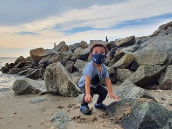 Full length of man on rocks at beach against sky
