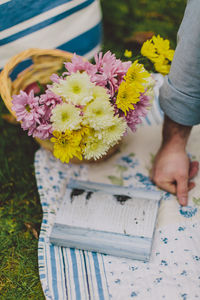 Cropped hand of man by book and flowers on picnic blanket