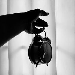 Close up of human hand holding alarm clock against curtain