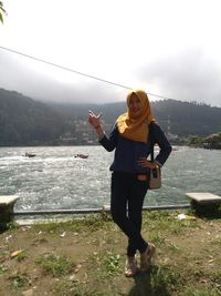 Portrait of smiling young woman wearing hijab while standing against lake