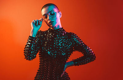 Young woman with shaved head wearing eyeglasses against orange background