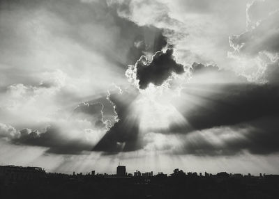 Sunlight streaming through clouds over silhouette landscape