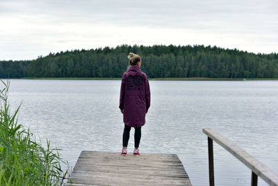 Rear view of woman standing on pier by lake against sky