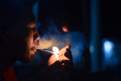 Side view of young man smoking cigarette at night