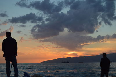 Rear view of silhouette man standing on beach against sky during sunset