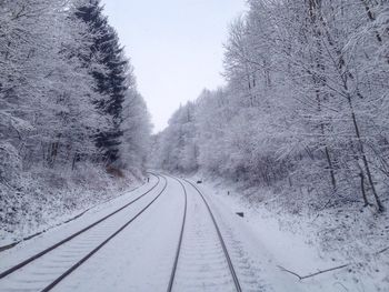 Snow covered railway tracks and bare trees against clear sky