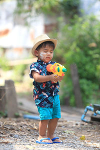 Cute boy holding toy gun standing outdoors