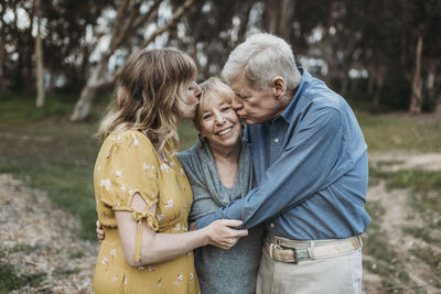 Senior mother being kissed by husband and adult daughter