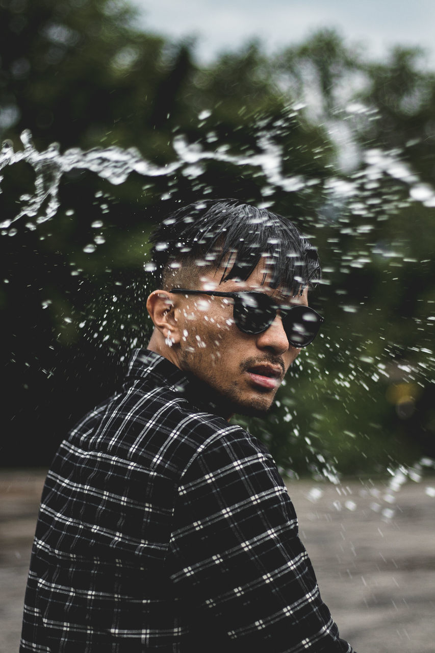 glasses, one person, young men, real people, lifestyles, young adult, tree, nature, leisure activity, water, portrait, motion, sunglasses, wet, day, waist up, casual clothing, focus on foreground, outdoors, rain