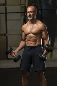 Shirtless man holding dumbbells in gym