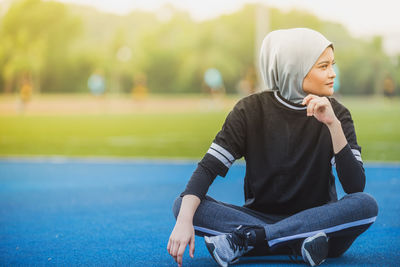 Thoughtful female athlete sitting at stadium