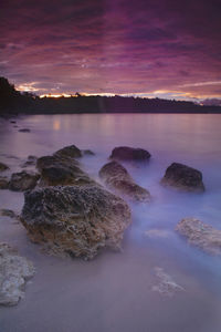 Rocks in sea against sky during sunset