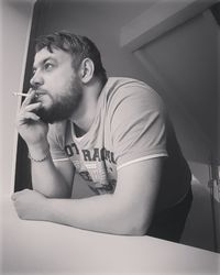 Close-up of man smoking cigarette by window at home