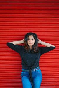 Portrait of beautiful young woman standing against red wall