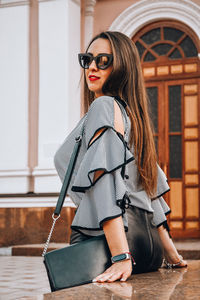 Portrait of young business woman sitting outside. girl in blouse and skirt on high heels. brunette 