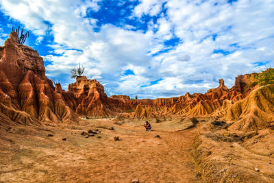 Woman crouching at tatacoa desert against cloudy sky