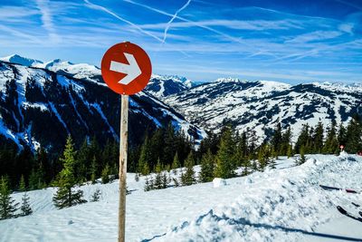 Road sign by snowcapped mountains against sky during winter