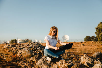 Young woman sitting on field against clear sky