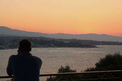 Rear view of man standing on mountain against sky during sunset