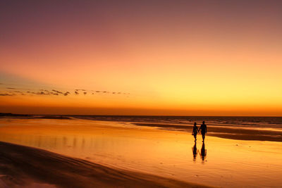 Silhouette couple on beach against sky during sunset
