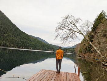 Rear view of man standing by lake against sky