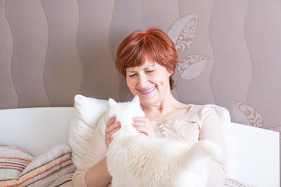 Portrait of smiling woman with cat sitting against wall