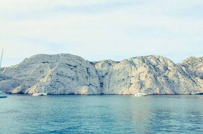 Scenic view of sea by mountain against sky